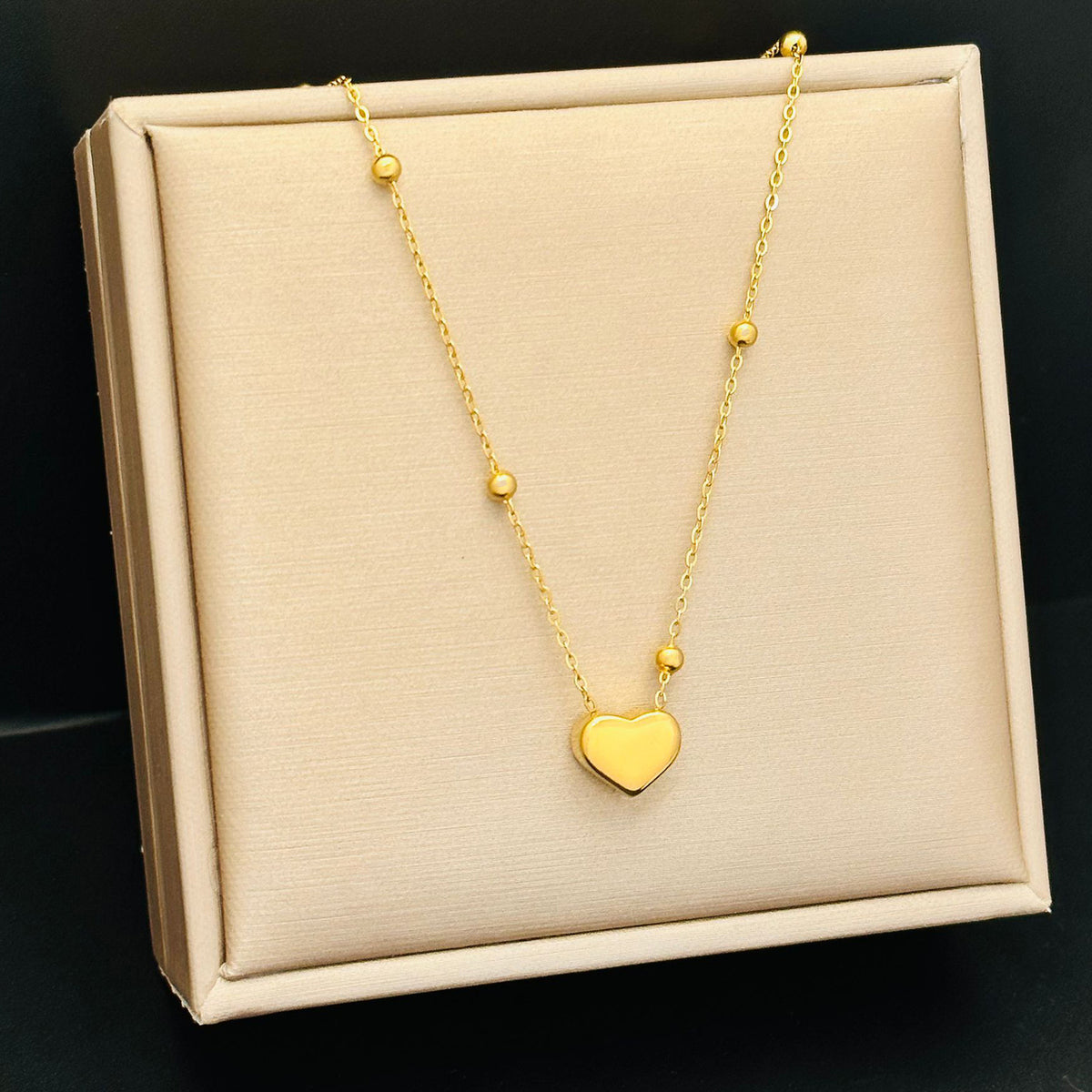Tiny Heart Necklace, gold heart pendant on a beaded chain, on a cream display tray